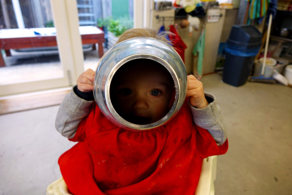 Image of a child peering through the middle of a rounded metal circle.